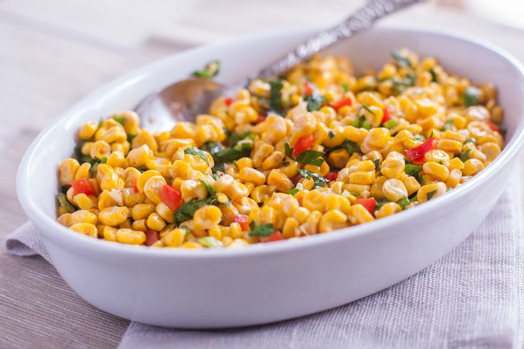 a white bowl filled with corn on top of a table next to a silver spoon