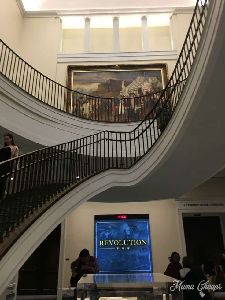 people are walking up and down an escalator in a building with a painting on the wall