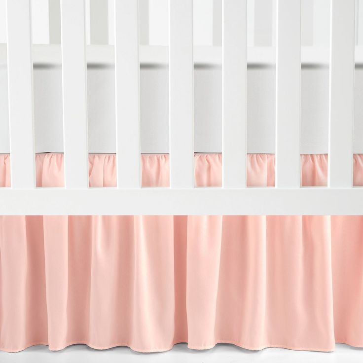 a white crib with pink bedding and curtains