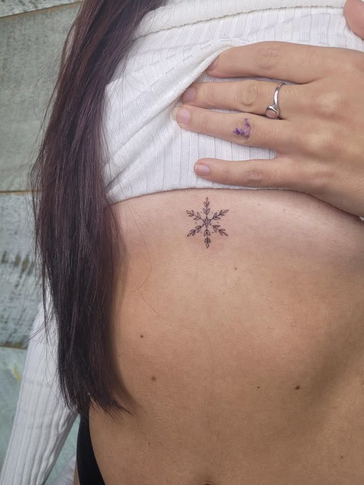 a woman's back with a small snowflake tattoo on it