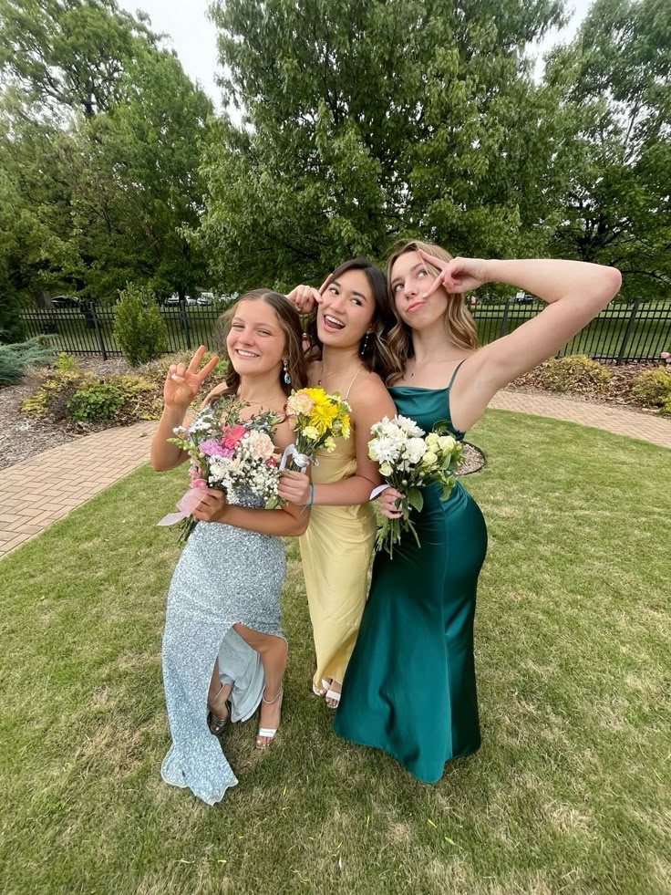 three young women posing for the camera in formal dresses and holding bouquets on their heads