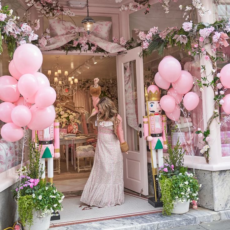 a woman standing in front of a store with pink balloons and decorations on the door