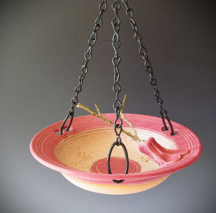 a pink and yellow bowl hanging from a black chain on a gray background with an empty plate in the foreground