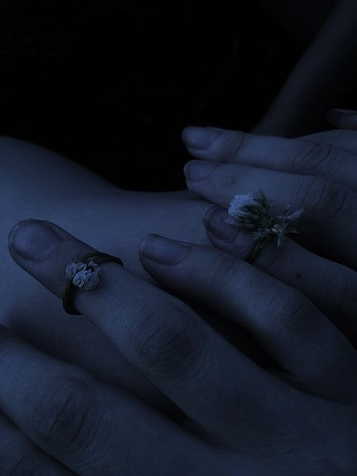 two hands with rings on their fingers and one holding a flower in the other hand