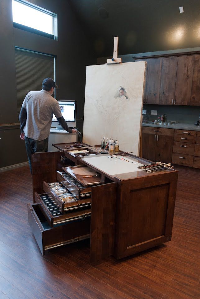 a man standing next to an easel in a room with hard wood flooring