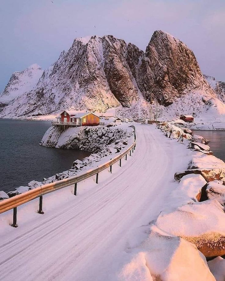 the road is covered in snow and there are some mountains on either side that look like they're coming out of the water