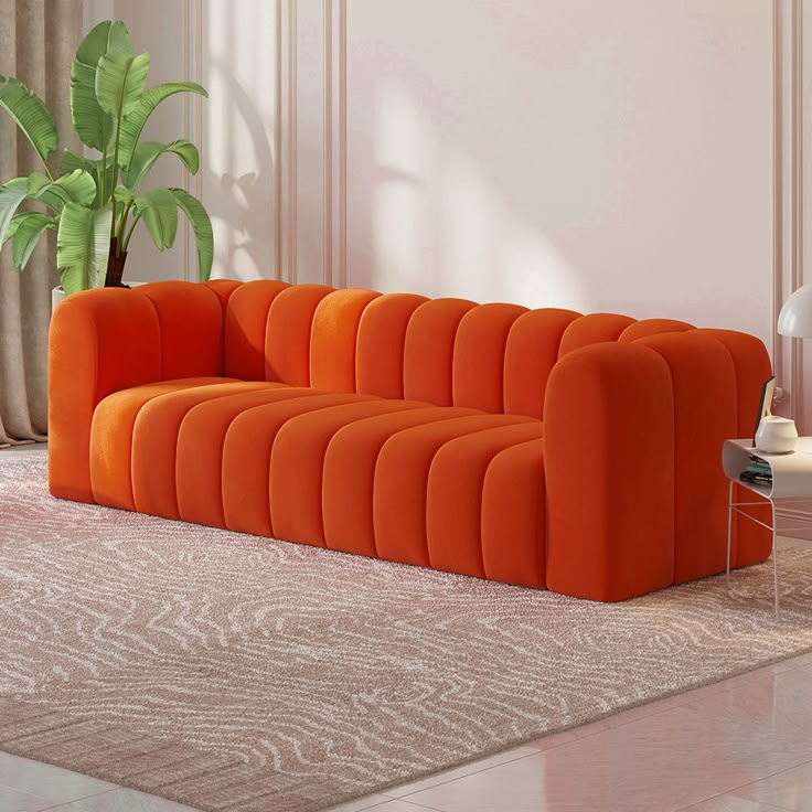 an orange couch sitting in the middle of a living room next to a potted plant