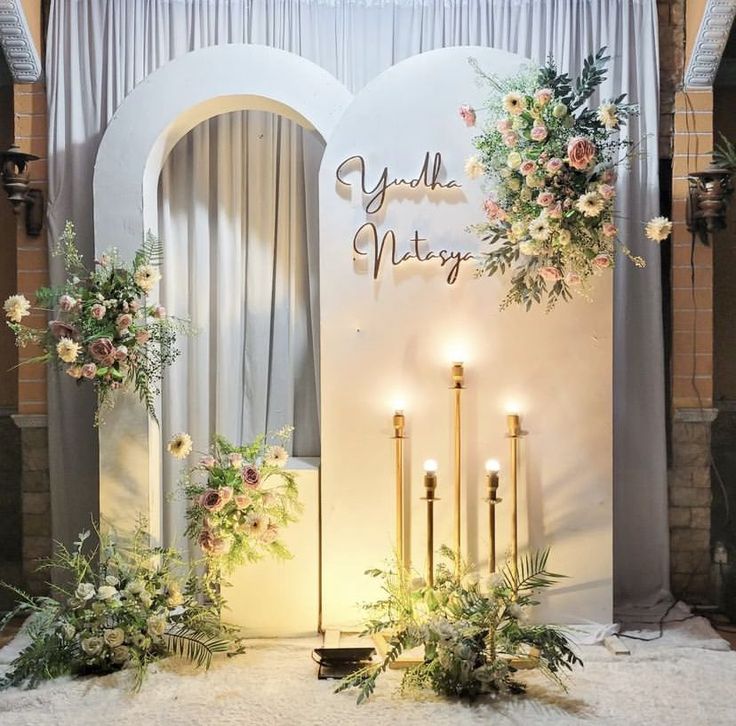 a decorated stage with candles, flowers and greenery in front of a white backdrop