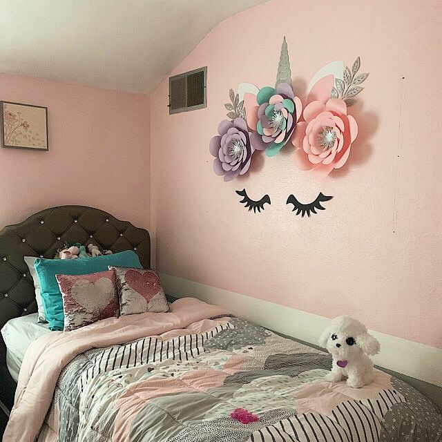 a bedroom decorated in pastel pink and grey with an unicorn themed wall hanging above the bed