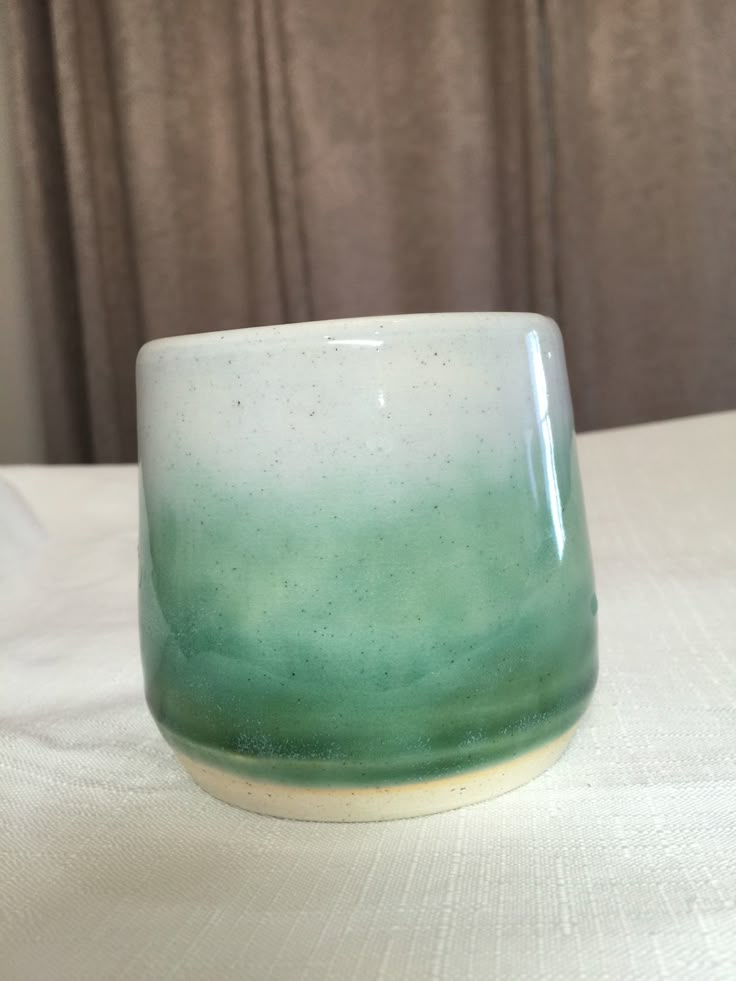 a green and white cup sitting on top of a table next to a curtained window