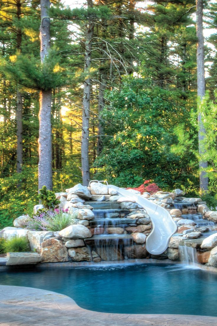 a pool with a slide in the middle of it and trees around it, surrounded by rocks