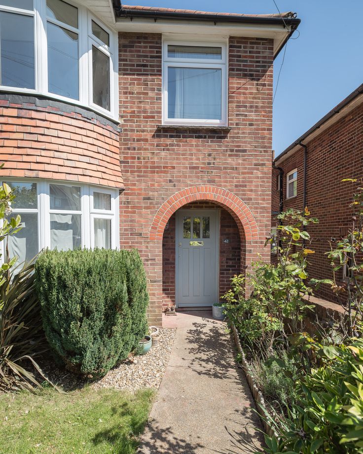 a brick house with an arched doorway and white trim on the front door is surrounded by greenery