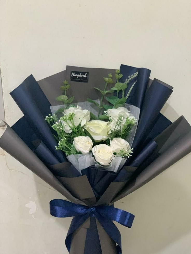 a bouquet of white roses wrapped in dark blue ribbon and tied with a bow on the wall