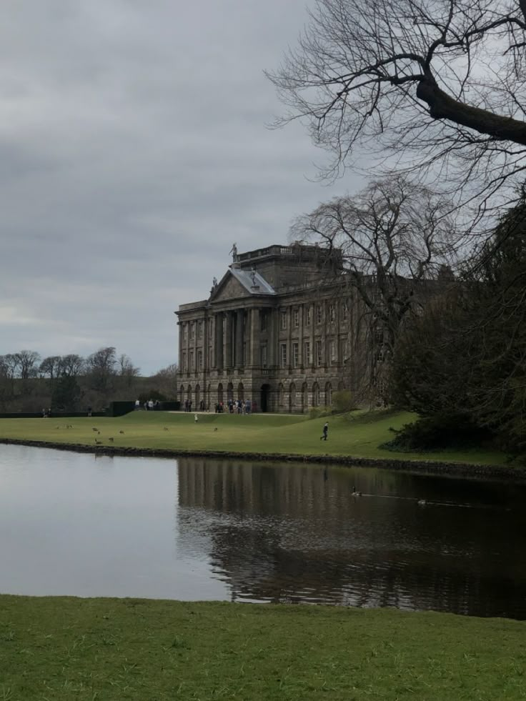 a large building sitting on top of a lush green field next to a lake in front of it