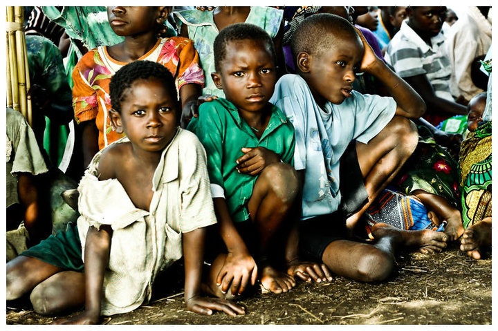 group of children sitting on the ground in front of a crowd