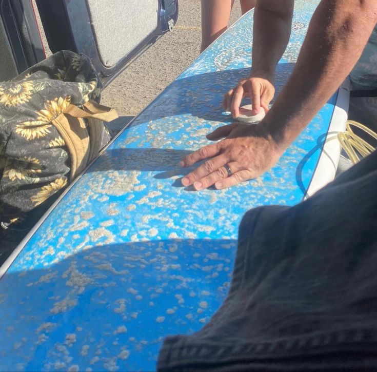 a man sanding on top of a blue surfboard next to another person with his hand on the board