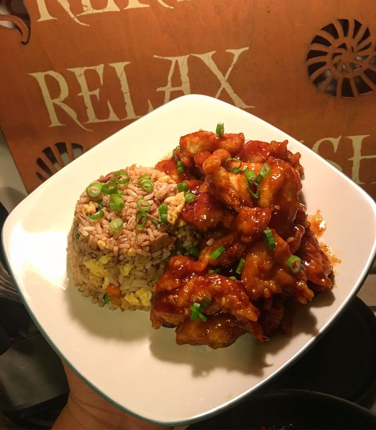 a white plate topped with rice covered in sauce and chicken next to a brown sign