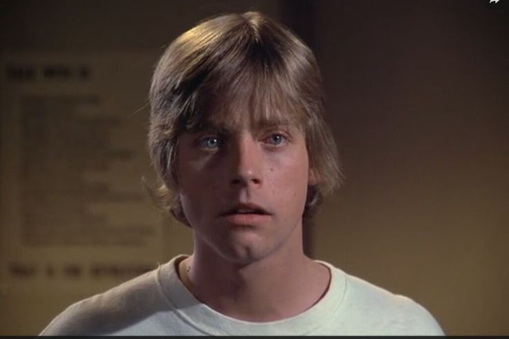 a young man with blonde hair wearing a white t - shirt and looking at the camera