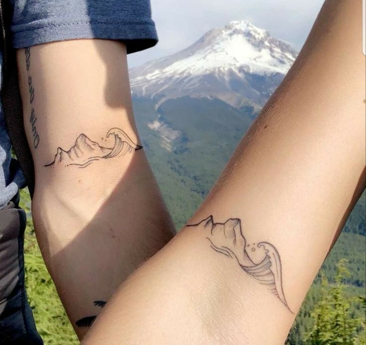 two people with matching tattoos on their arms and legs in front of a mountain range