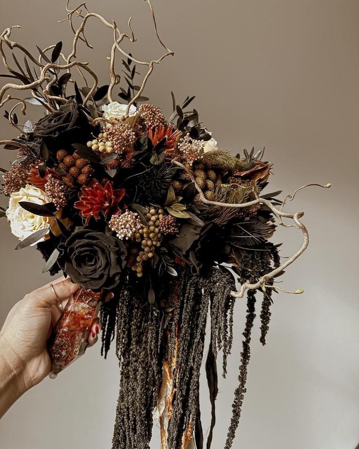 a person holding up a bouquet made out of branches and dried flowers in front of a gray background