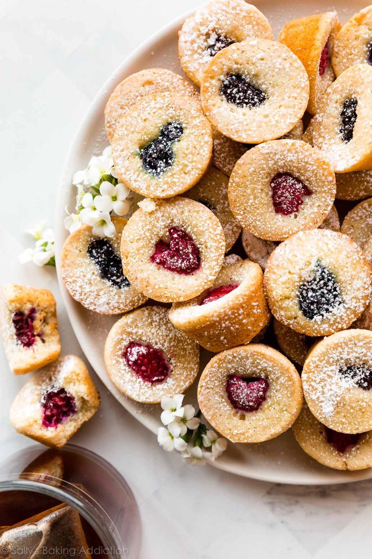 a white plate topped with small pastries covered in powdered sugar next to flowers