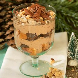 a dessert in a glass on top of a table next to a christmas tree and pine cones