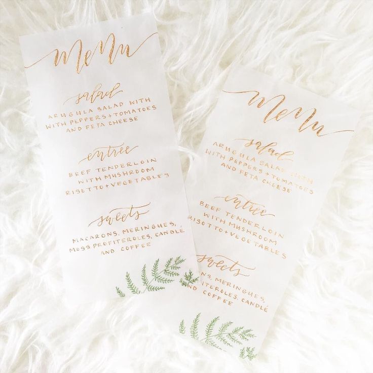 two white and gold wedding programs with greenery on them