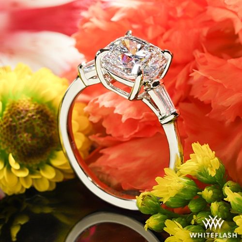 a close up of a diamond ring with flowers in the foreground and an orange flower behind it