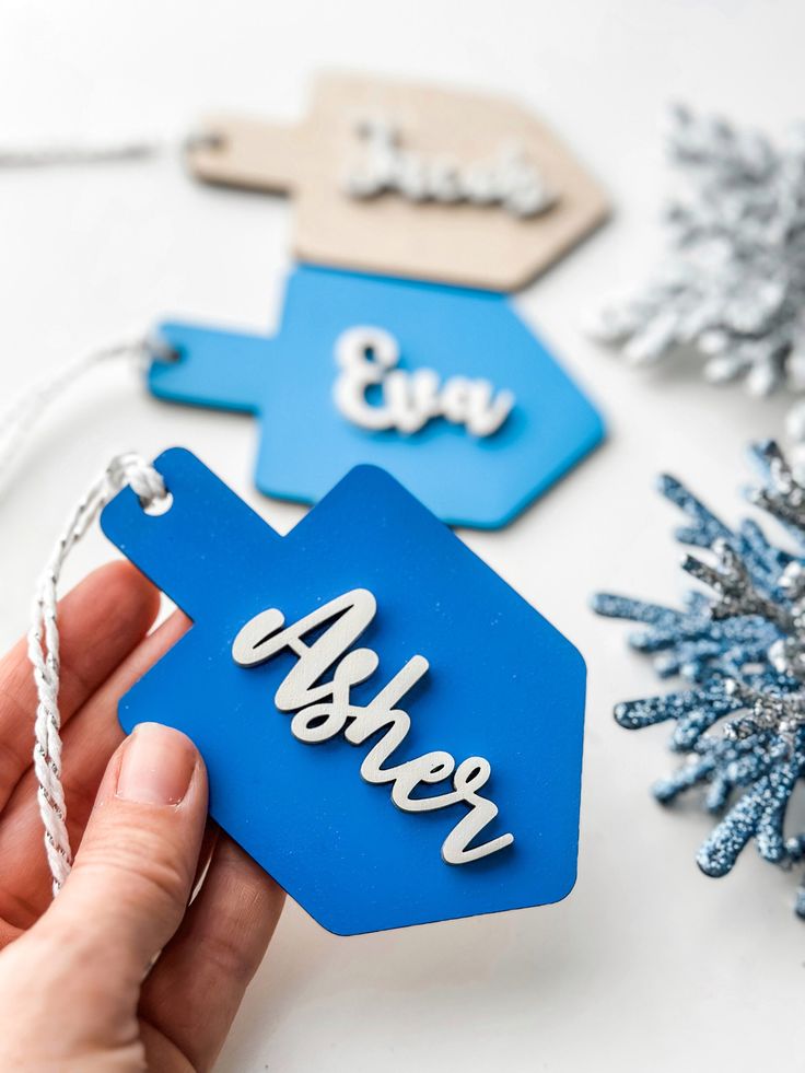 a hand holding an ornament with the word winter on it and snowflakes in the background