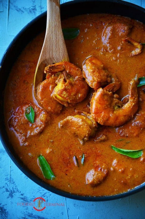 a pan filled with shrimp and sauce on top of a blue table next to a wooden spoon