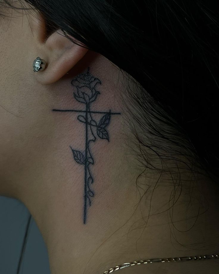 a woman's neck with a cross and rose tattoo on her left side behind the ear