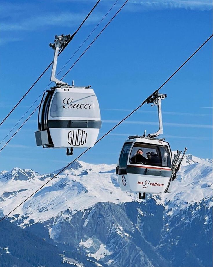 two gondolas with people riding on them above the snow covered mountain range in the distance