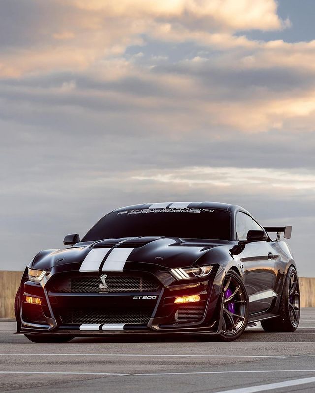 a black sports car with white stripes parked on the side of an airport tarmac