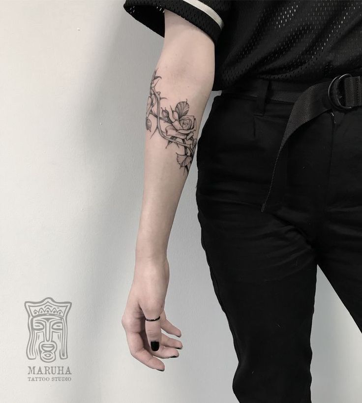 a person with a flower tattoo on their left arm holding onto a wall and wearing black pants