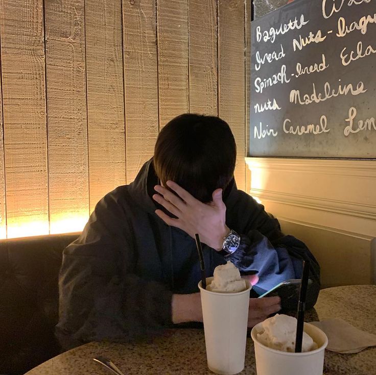 a man sitting at a table with two cups in front of him, covering his face