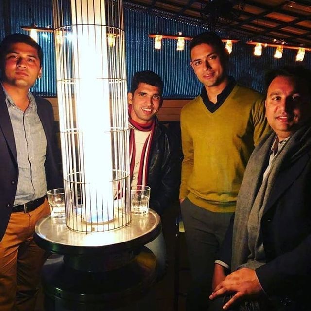 three men are standing next to a tall glass vase in a room with lights hanging from the ceiling