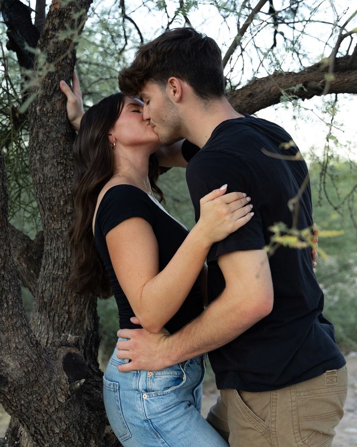 a man and woman kissing in front of a tree with their arms around each other