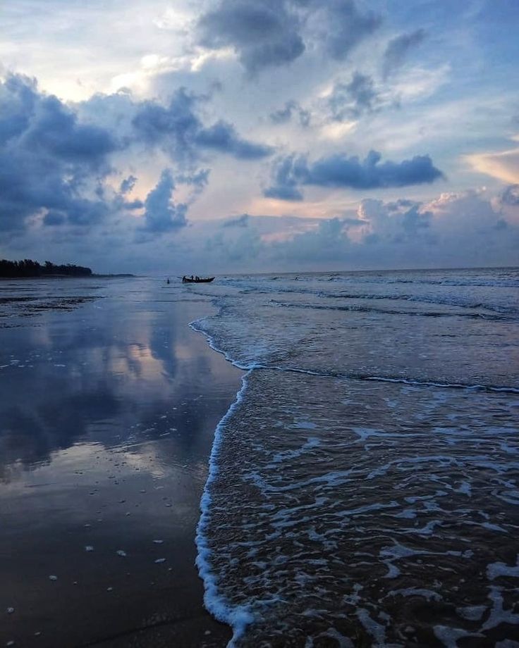 there is a boat that is on the beach in the water and clouds are reflected in the wet sand