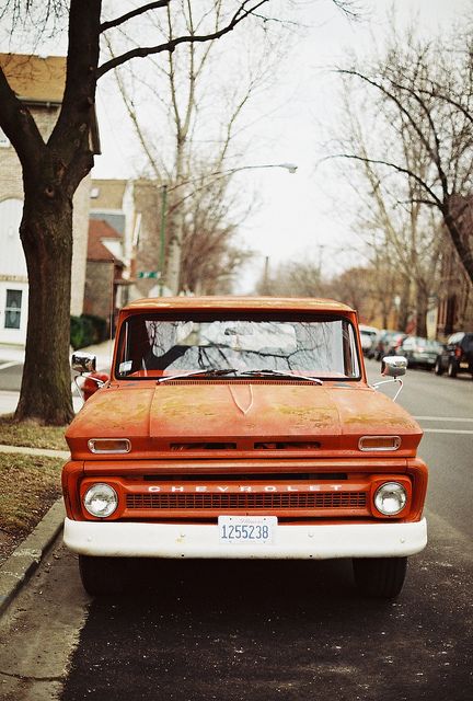 an orange truck parked on the side of a road next to a tree and buildings