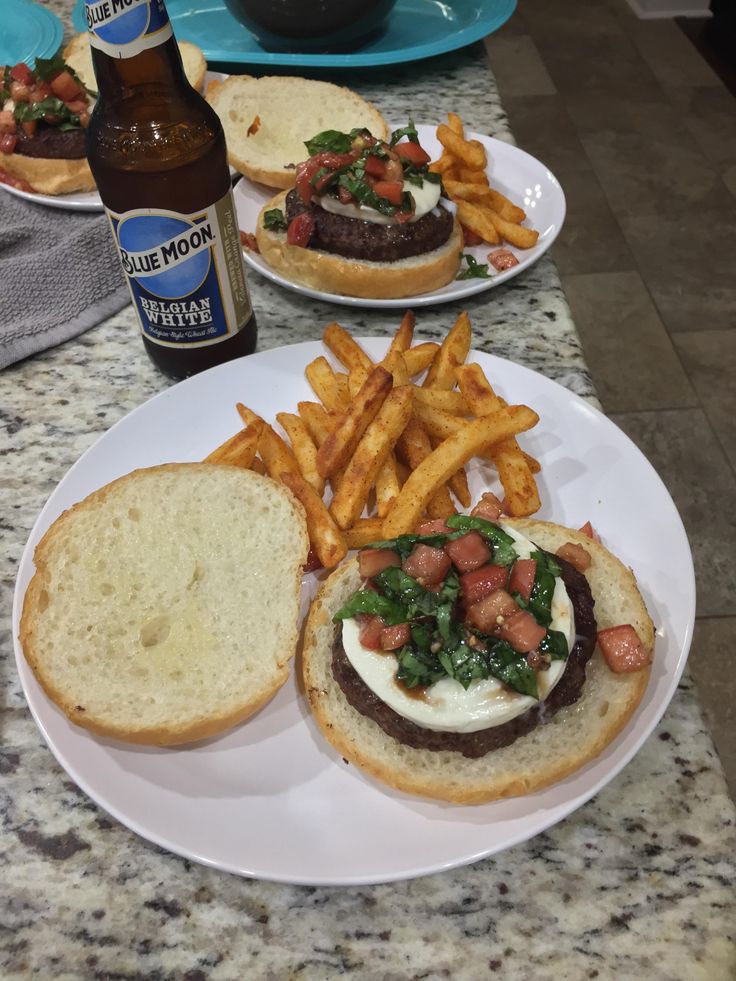 two plates with sandwiches and french fries on the table next to bottles of blue moon beer