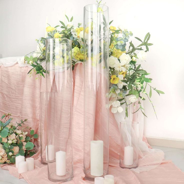 flowers and candles are arranged in vases on a pink tablecloth with white roses