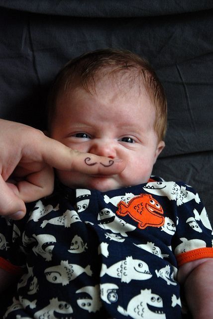 a baby is being held up to the camera by someone's hand with an orange nose ring on it