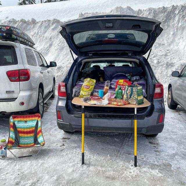 two cars parked in the snow with their back doors open and food laid out on top