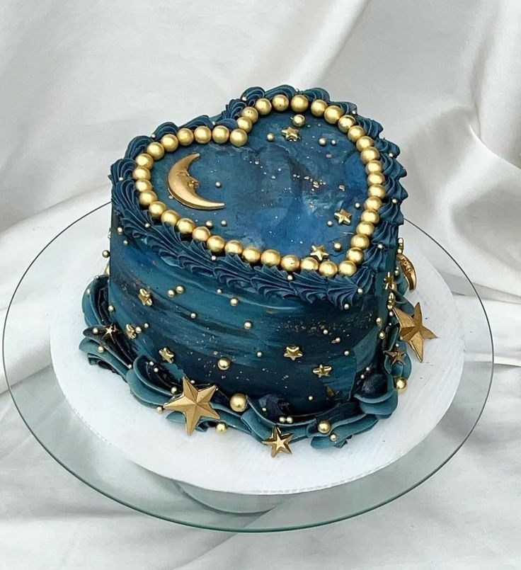 a blue cake with gold stars and a heart shaped decoration on the top is sitting on a glass plate