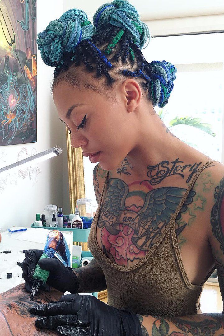 a woman getting her hair done by another woman with tattoos on her arms and shoulder