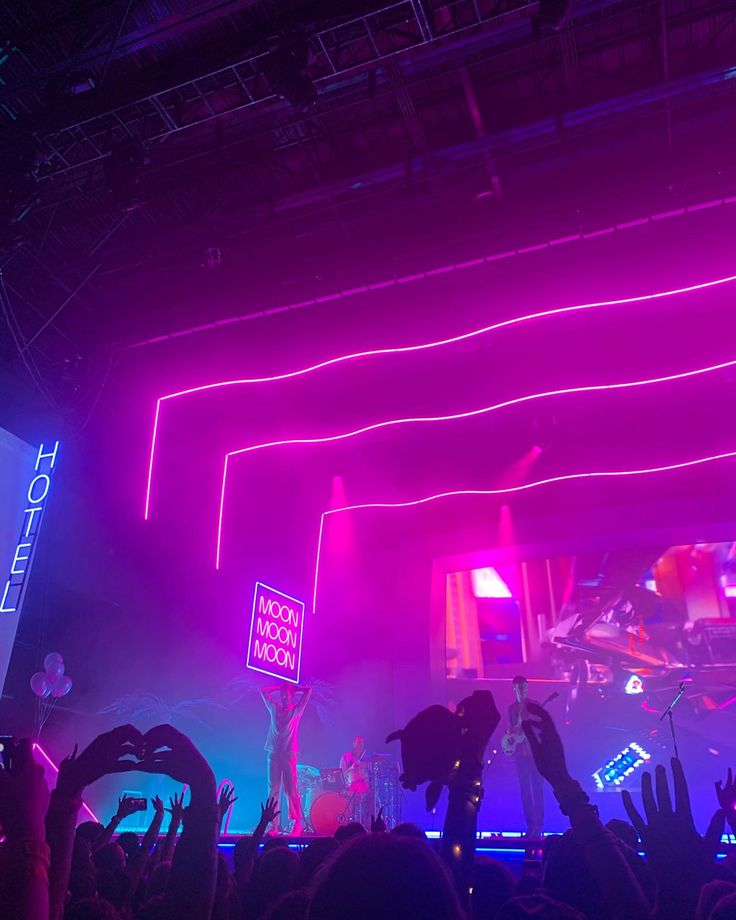 a crowd of people at a concert with their hands up in front of the stage lights