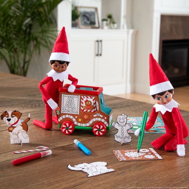 two elfs are sitting on the table with paper cutouts and crayons