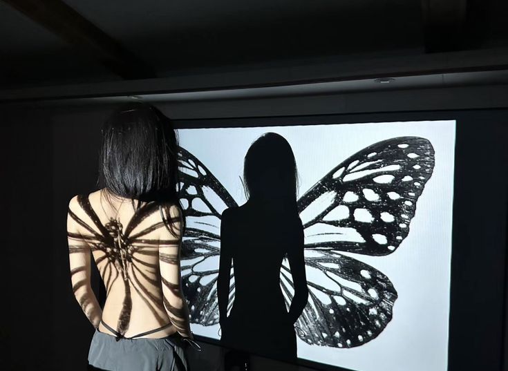 a woman standing in front of a butterfly projected on a wall with her back to the camera