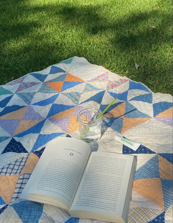 an open book sitting on top of a quilt next to a vase filled with flowers