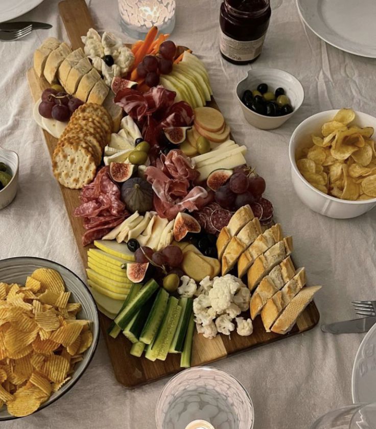 a wooden platter filled with cheese, crackers and other snacks on top of a white table cloth